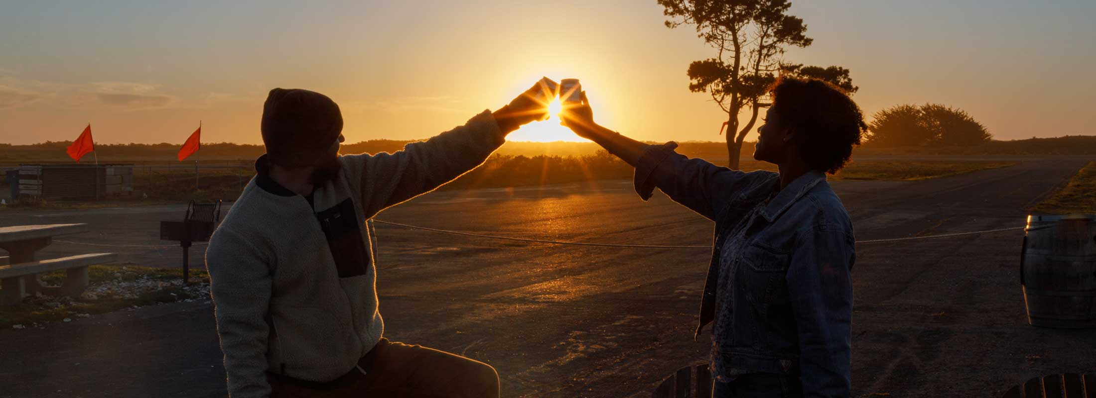 Two people join hands to form a heart around the light of the setting sun
